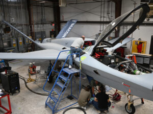 Model 437 aircraft sits inside hangar with cockpit open and multiple aircraft technicians working on it.